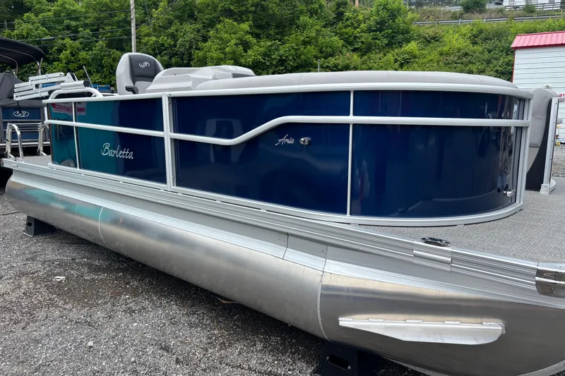 Slide: The Image of 2025 Barletta Aria 20L pontoon boat, blue exterior, parked on gravel lot. - 2