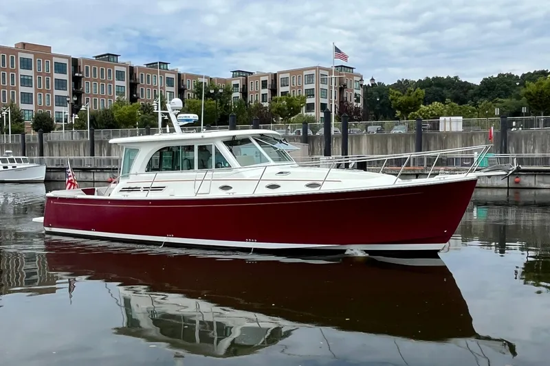 Slide: The Image of 2017 Back Cove 41 boat with red hull docked in a marina, urban backdrop. - 123