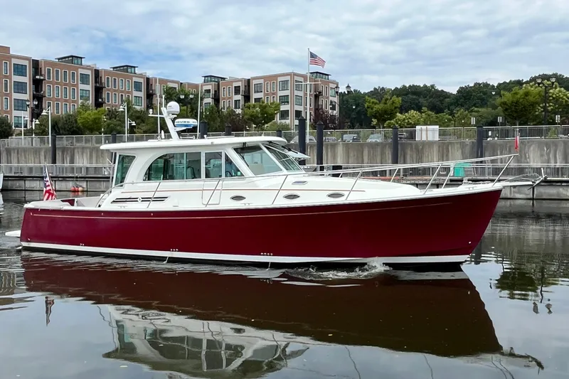 Slide: The Image of 2017 Back Cove 41 boat with red hull docked in a marina, modern buildings in background. - 2