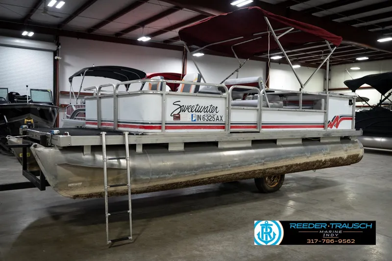 Slide: The Image of 1993 Godfrey Sweetwater pontoon boat with red canopy in indoor showroom. - 3