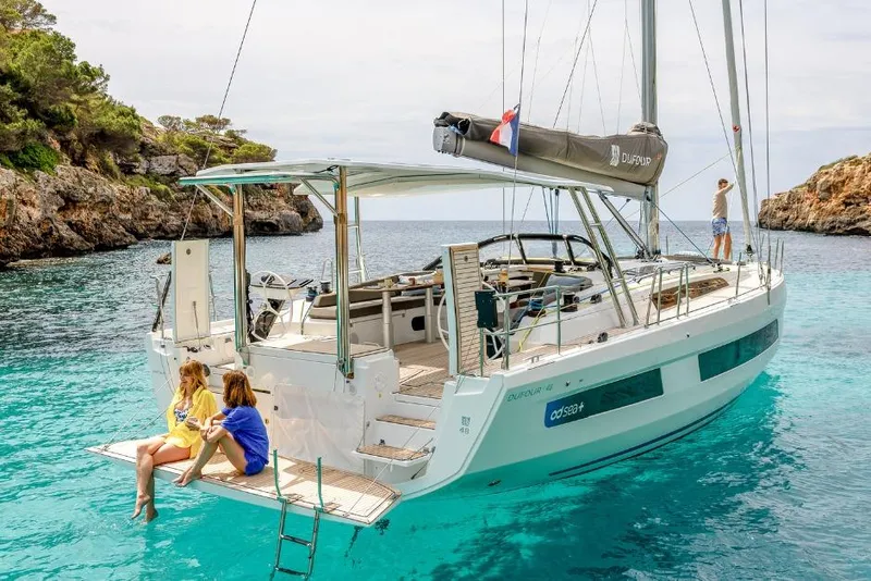Slide: The Image of 2026 Dufour 48 yacht anchored in a scenic cove with people relaxing onboard. - 27
