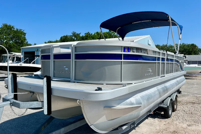 Slide: The Image of 2023 Bennington SX23 pontoon boat on trailer, blue canopy, parked outdoors. - 2