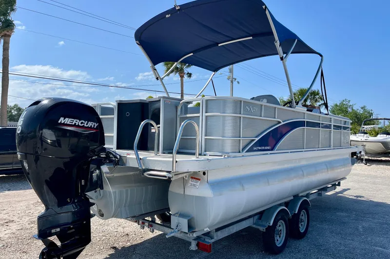 Slide: The Image of 2023 Bennington SX23 pontoon boat with Mercury engine, parked on a trailer under a blue sky. - 6