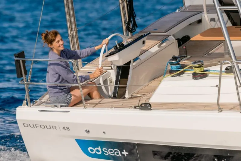 Slide: The Image of Woman steering 2026 Dufour 48 yacht on open sea, smiling, sunny day. - 11