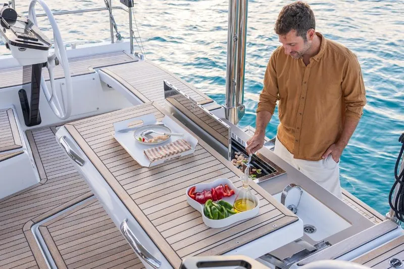 Slide: The Image of Man cooking on a 2026 Dufour 48 yacht with fresh vegetables and sea view. - 13
