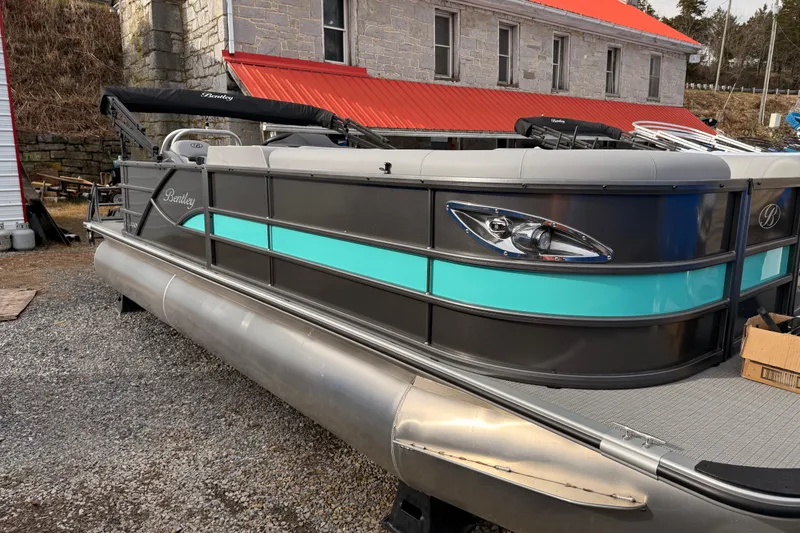 Slide: The Image of 2025 Bentley Pontoons Legacy Cruise XL with teal accents, parked near a stone building. - 6