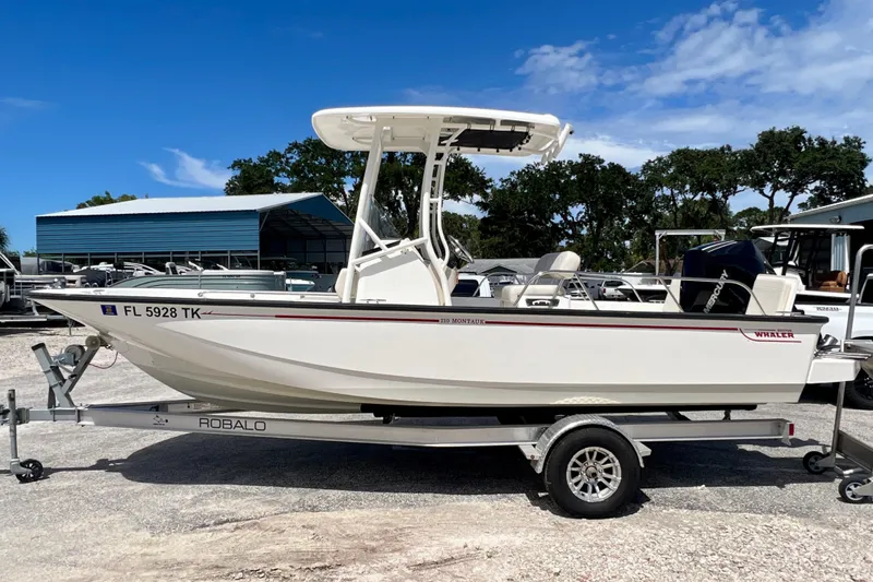Slide: The Image of 2023 Boston Whaler 210 Montauk boat on trailer, parked outdoors under blue sky. - 5