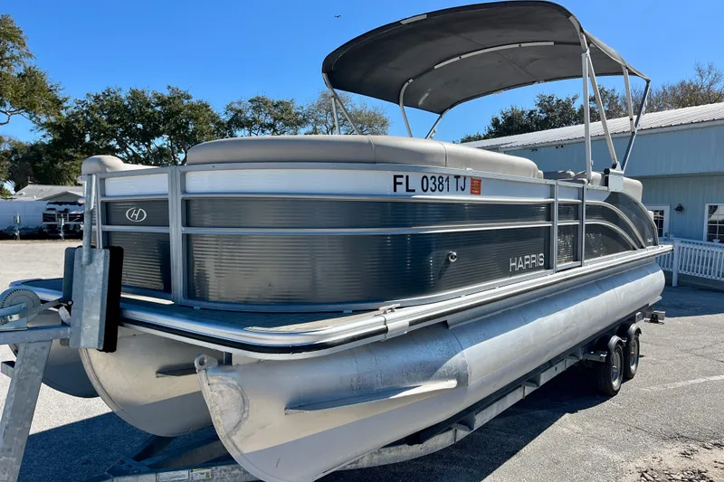 Slide: The Image of 2023 Harris Cruiser 230 pontoon boat on trailer, parked outdoors under clear blue sky. - 23