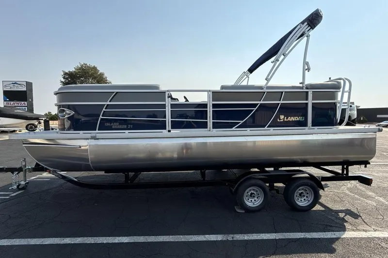 Slide: The Image of 2026 Landau Island Breeze 21 C pontoon boat on trailer, parked outdoors. - 2