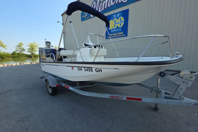 The Image of 2022 Boston Whaler 150 Montauk boat on trailer, parked near a dealership. - 0