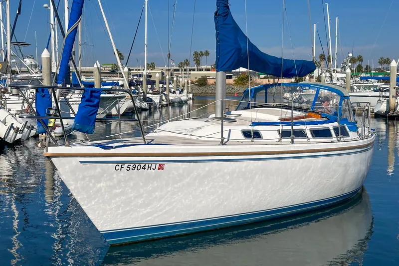 Slide: The Image of 1984 Catalina 30 sailboat docked in marina, featuring blue sail covers and calm water reflections. - 11