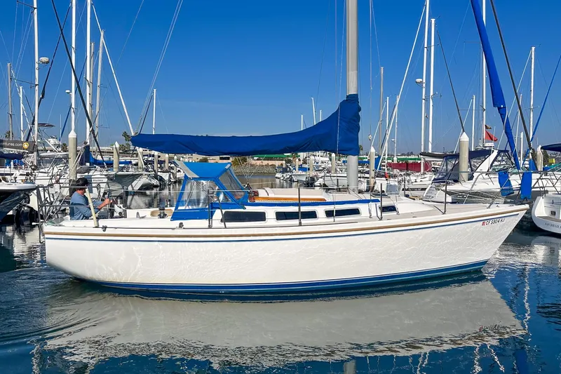 Slide: The Image of 1984 Catalina 30 sailboat docked in marina, featuring blue accents and clear sky background. - 18