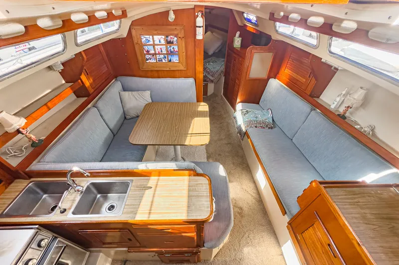 Slide: The Image of 1984 Catalina 30 sailboat interior with cozy seating, dining table, and compact kitchen area. - 49