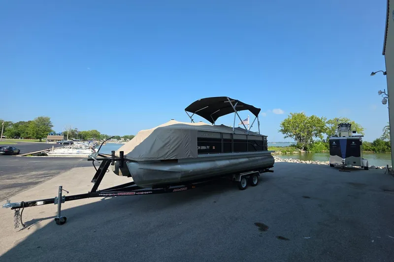 Slide: The Image of 2015 Crest III 230 SL pontoon boat on trailer, parked near a lake under clear blue sky. - 6