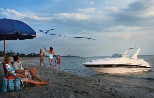 Slide: The Image of Family enjoying beach near 2010 Larson Cabrio 274 boat, flying kites under a blue umbrella. - 2