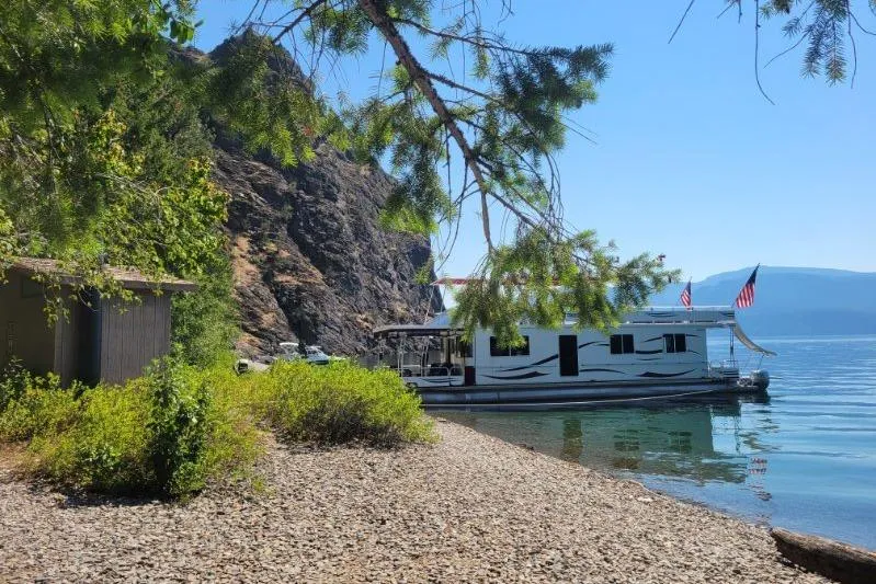 Slide: The Image of Houseboat Sailabration 64 (2015) docked by rocky shore with trees and mountains. - 42