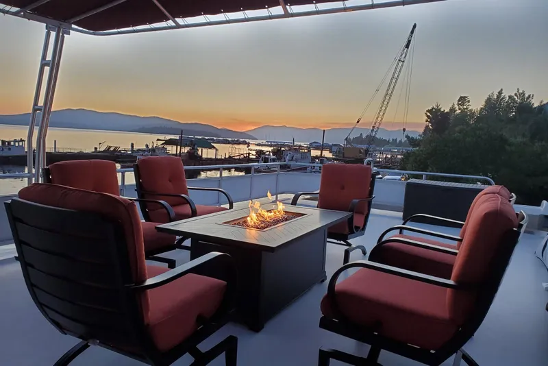 Slide: The Image of Luxurious Sailabration 64 houseboat deck with fire pit, red chairs, and scenic sunset view. - 44