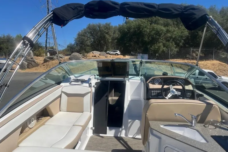 Slide: The Image of 2020 Four Winns V255 boat interior with seating, steering wheel, and sink under a clear blue sky. - 6