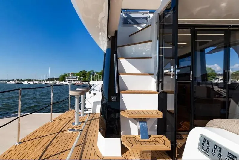 Slide: The Image of 2023 Galeon 470 Sky yacht deck with wooden stairs and glass doors, docked by the water. - 12