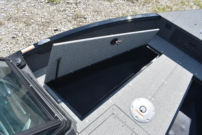 Slide: The Image of 2026 Lund 1800 Explorer Sport boat storage compartment with open hatch on gravel surface. - 16