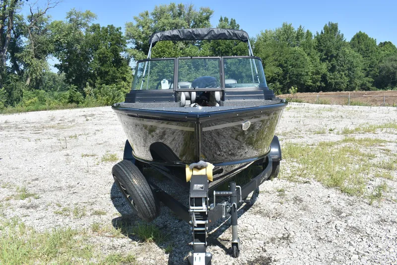Slide: The Image of 2026 Lund 1800 Explorer Sport boat on trailer, parked on gravel with trees in background. - 2