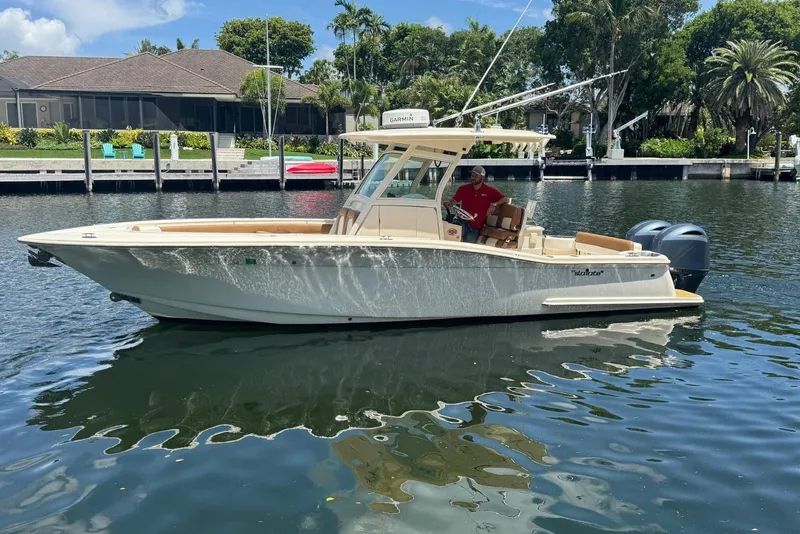 Slide: The Image of 2013 Scout 275 LXF boat on calm water, with lush greenery and houses in the background. - 10