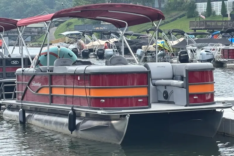 The Image of 2025 Bentley Pontoons Legacy Navigator docked, featuring red and orange accents, with canopy. - 0