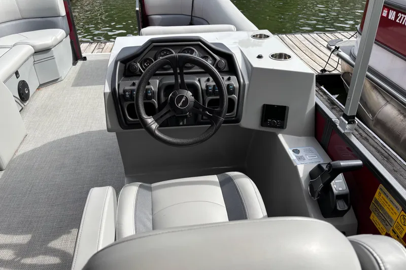 Slide: The Image of 2025 Bentley Pontoons Legacy Navigator dashboard with steering wheel and controls, docked by water. - 5