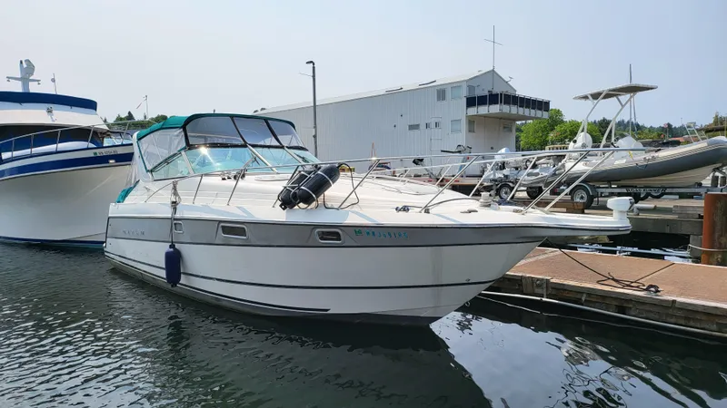 The Image of 1994 Maxum 3200 SCR boat docked at marina, white hull, blue canopy, calm water. - 0