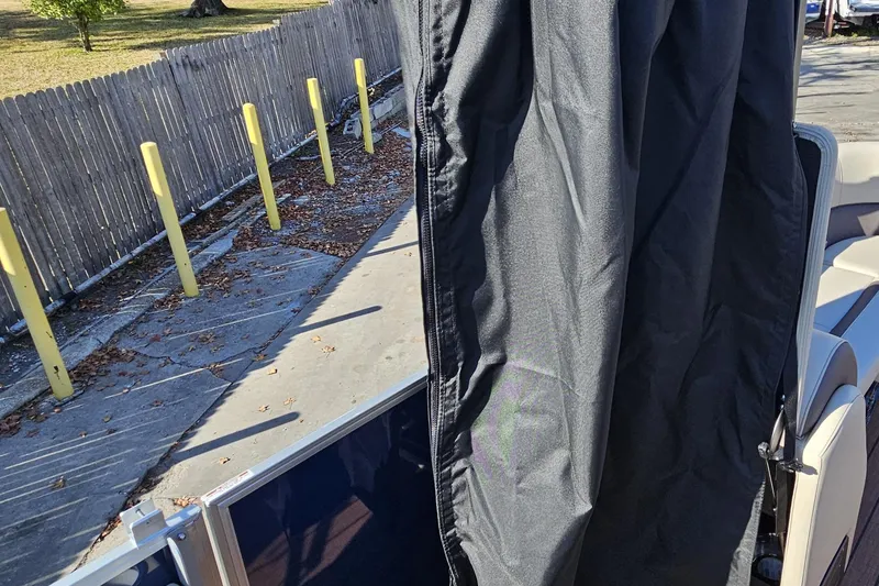 Slide: The Image of 2025 Bentley Pontoons Legacy 243 Swingback with black cover, parked near a wooden fence. - 30