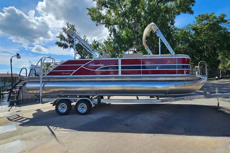 Slide: The Image of 2025 Bentley Pontoons Legacy 243 Swingback on trailer, parked outdoors under a clear sky. - 6