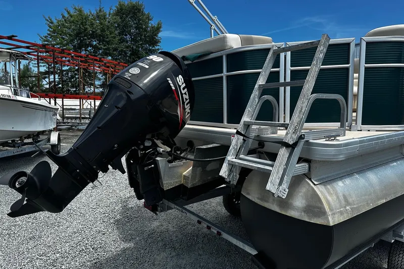 Slide: The Image of 2016 Godfrey Sweetwater 2086 Pontoon with Suzuki outboard motor and ladder, parked on gravel. - 2