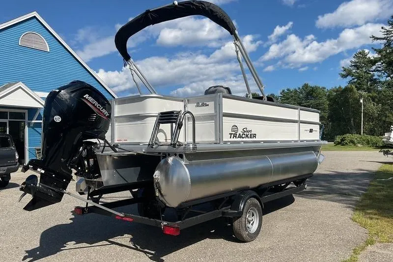 Slide: The Image of 2026 Sun Tracker PB 18 DLX pontoon boat on trailer, parked outdoors under blue sky. - 6