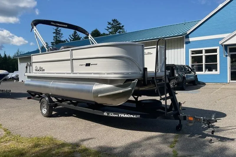 Slide: The Image of 2026 Sun Tracker PB 18 DLX pontoon boat on trailer, parked outside blue building. - 9