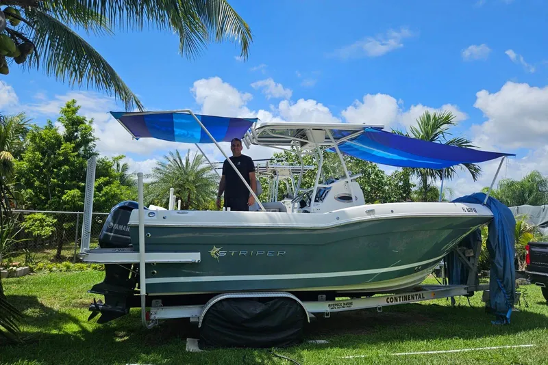 Slide: The Image of 2020 Striper 220 Center Console boat on trailer, surrounded by palm trees and blue sky. - 63