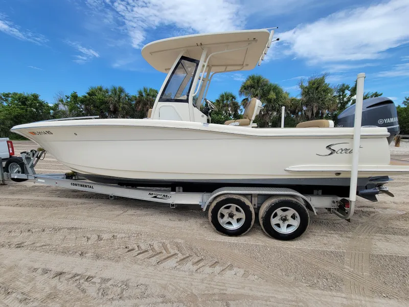 Slide: The Image of 2018 Scout 235XSF boat on trailer, parked on sandy terrain under a clear blue sky. - 2