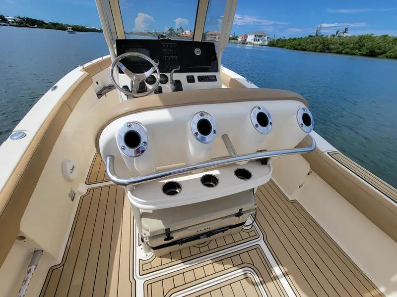 Slide: The Image of 2018 Scout 235XSF boat interior with steering wheel and rod holders on a sunny day. - 5