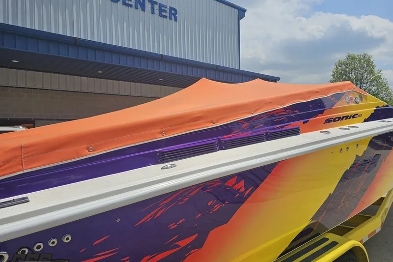 Slide: The Image of 2003 Sonic USA 31SS speedboat with vibrant graphics and orange cover, parked near a building. - 32