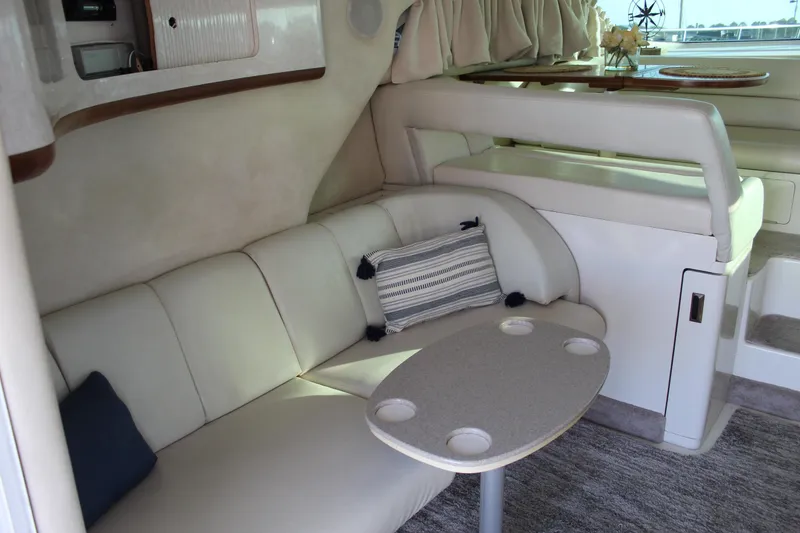 Slide: The Image of 1997 Sea Ray 400 Sedan Bridge interior with beige seating, small table, and decorative pillows. - 13