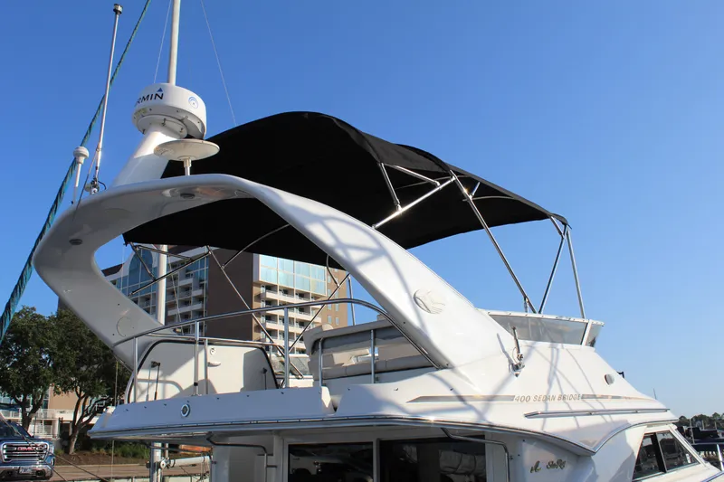 Slide: The Image of 1997 Sea Ray 400 Sedan Bridge yacht with black canopy, docked near modern buildings. - 6