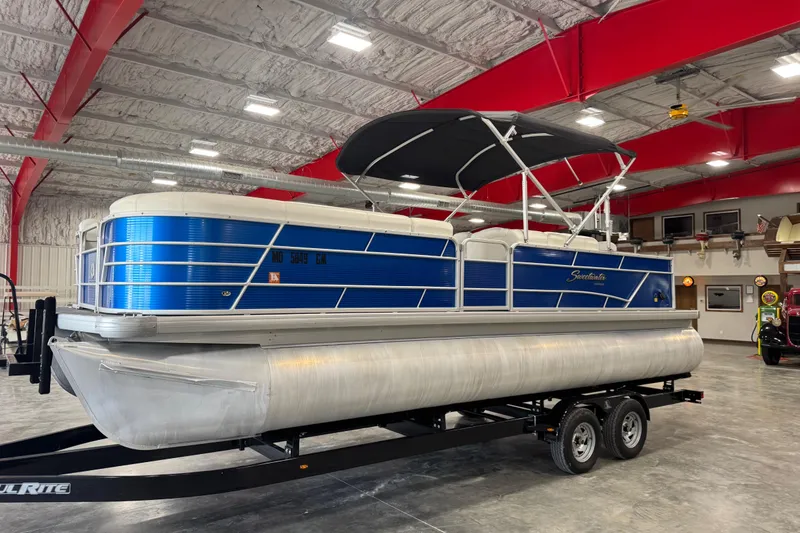 Slide: The Image of 2019 Sweetwater 2486 pontoon boat with blue exterior, parked indoors on a trailer. - 1