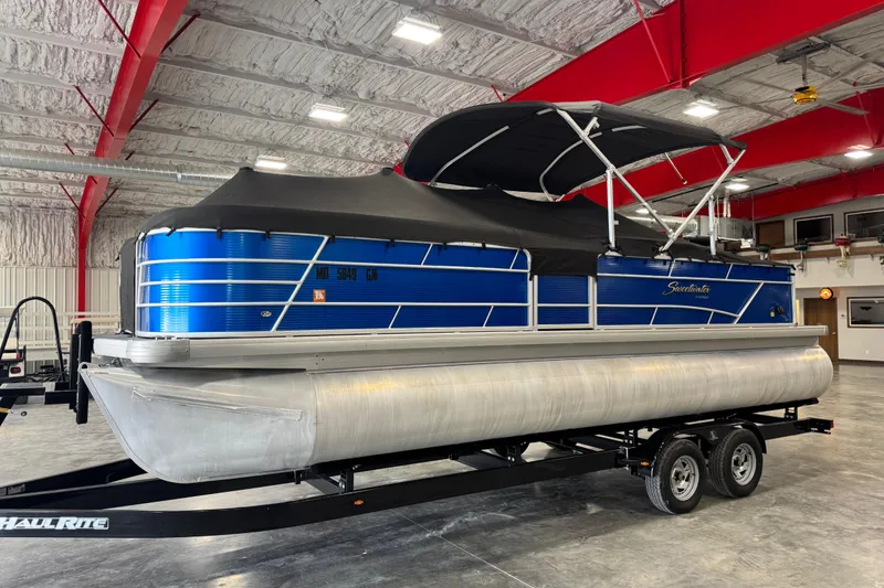 Slide: The Image of 2019 Sweetwater 2486 pontoon boat in a warehouse, featuring a blue exterior and black canopy. - 15