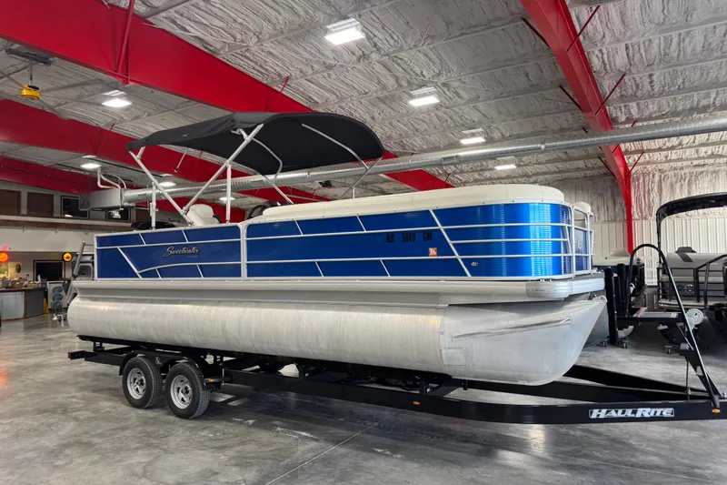 Slide: The Image of 2019 Sweetwater 2486 pontoon boat with blue exterior in a spacious indoor showroom. - 2