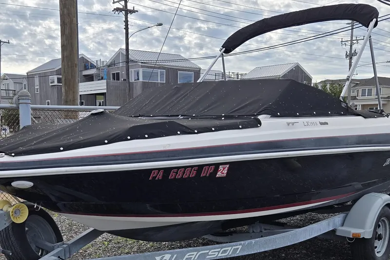 Slide: The Image of 2014 Larson LX 195S IO boat on trailer, covered, with bimini top, parked near coastal homes. - 15