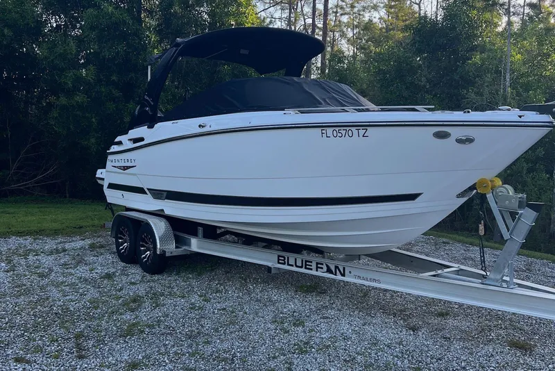 Slide: The Image of 2025 Monterey 255 Super Sport boat on trailer, parked on gravel with trees in background. - 2