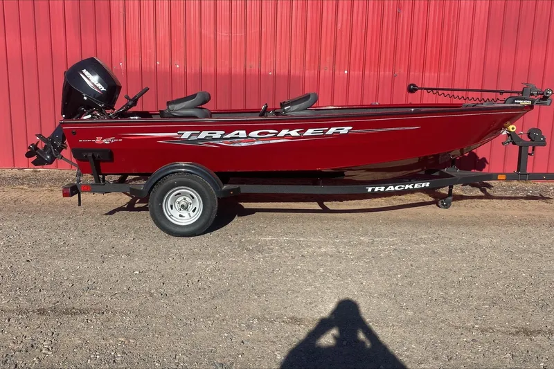 The Image of 2025 Tracker Super Guide V-16 T boat on trailer, red exterior, parked by red wall. - 0