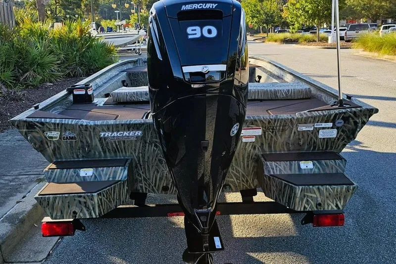 Slide: The Image of 2026 Tracker Grizzly 1860 CC boat with Mercury 90 engine, camo design, parked outdoors. - 4