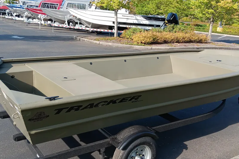 Slide: The Image of 2026 Tracker Grizzly 1648 Utility boat on trailer in parking lot, surrounded by trees and other boats. - 2
