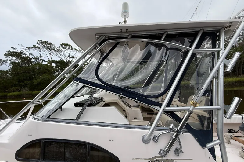 Slide: The Image of 2003 Grady-White Sailfish 282 boat with metal framework and clear enclosure, docked near trees. - 6