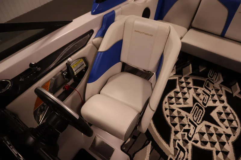 Slide: The Image of 2011 Nautique 210 SUPER AIR boat interior with white and blue seating, steering wheel, and custom carpet. - 26
